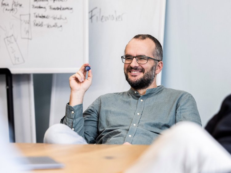 Teammitglied der Alpenblickdrei Werbeagentur zeigt lächelnd auf ein Flipchart bei einer lockeren Präsentation.