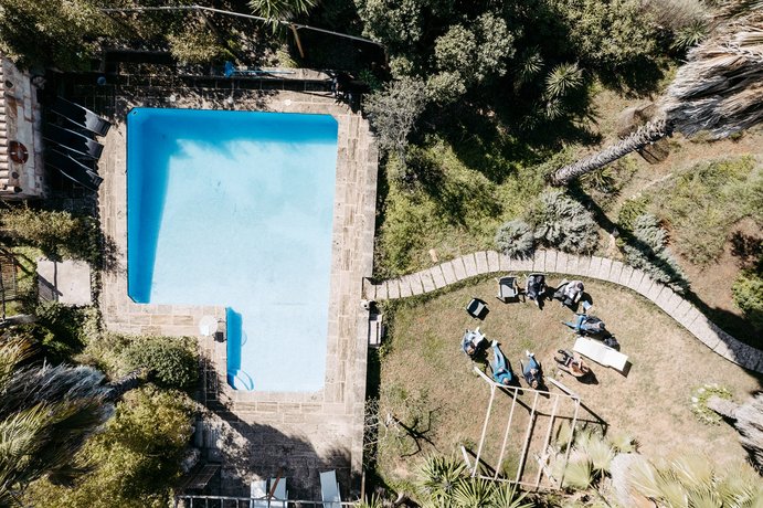 Rechteckiger Pool in Naturstein eingefasst, gelegen inmitten von Bäumen und natürlicher Landschaft auf Mallorca, aus der Vogelperspektive fotografiert.