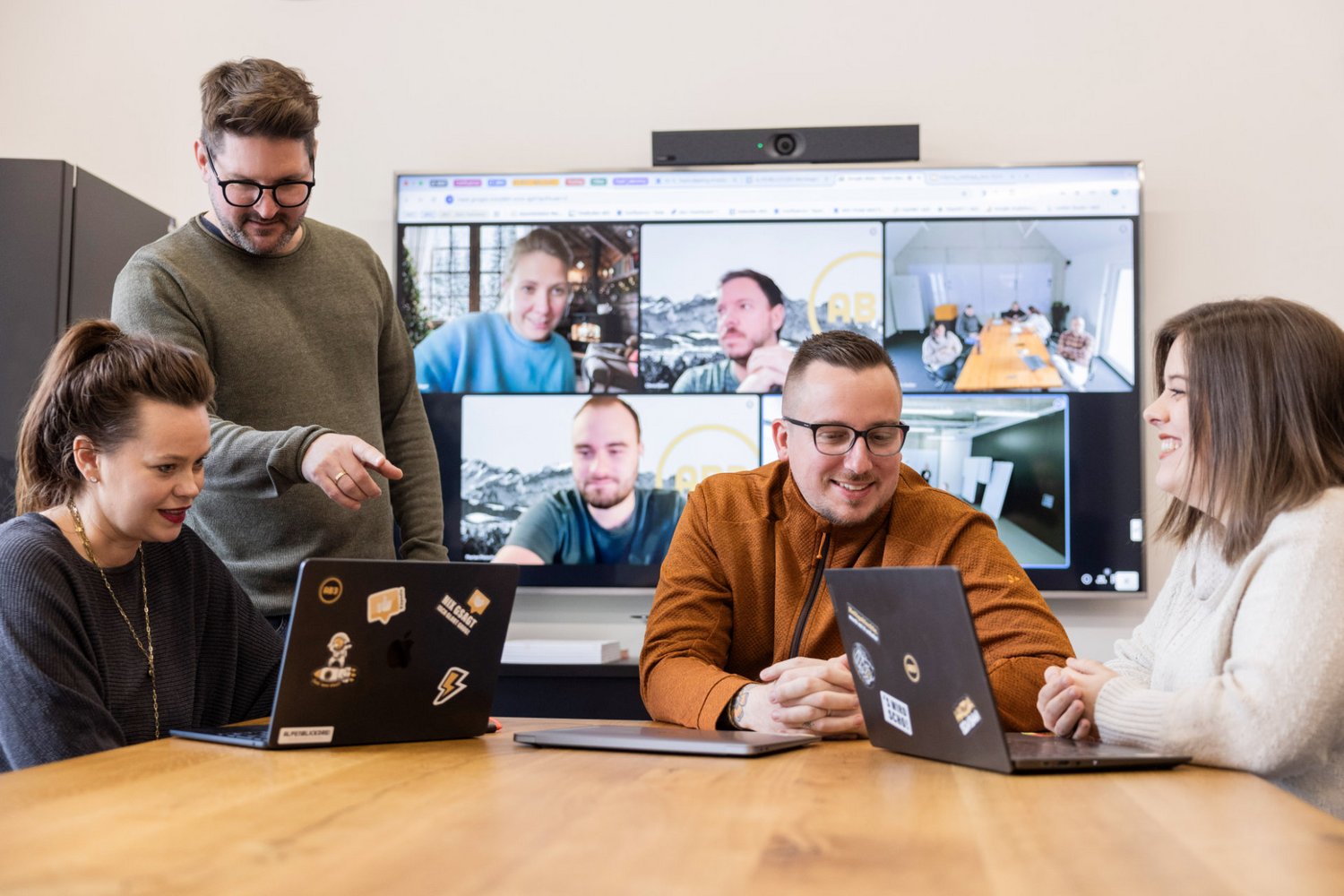 Mehrere Teammitglieder der Alpenblickdrei Werbeagentur diskutieren konzentriert am Tisch mit offenem Laptop.
