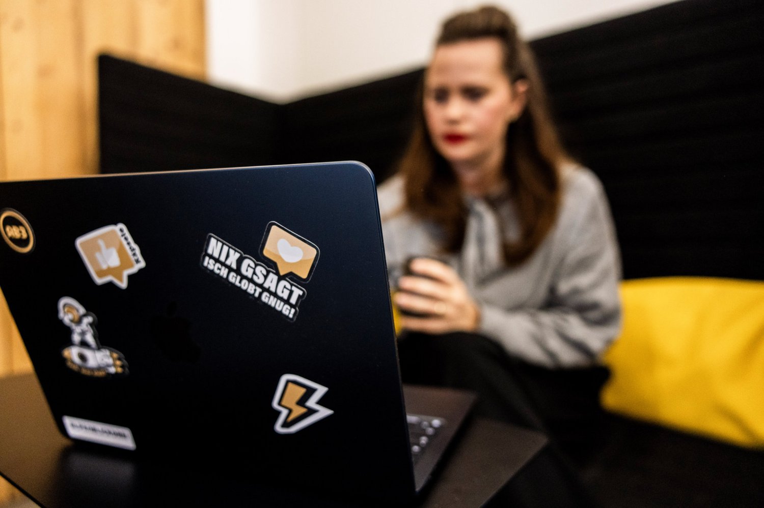 Arbeiten mit Fokus Mitarbeiterin der Alpenblickdrei Werbeagentur arbeitet konzentriert am Laptop auf einem gelben Sofa.