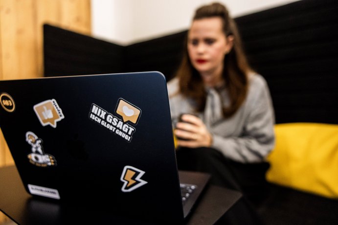 Mitarbeiterin der Alpenblickdrei Werbeagentur arbeitet konzentriert am Laptop auf einem gelben Sofa.