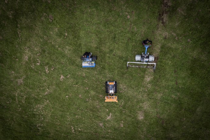 Drei autonome Rasenmäher fahren auf einem grünen Feld und mähen das Gras.