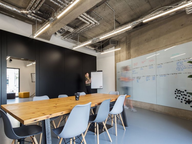 Konferenzraum Großer Meetingraum mit langem Tisch, weißen Stühlen, beschreibbarer Glaswand, Flipchart und einer Person bei Präsentation.