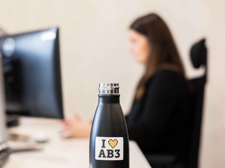 Eine schwarze Trinkflasche mit der Aufschrift „I ♥ AB3“ steht auf einem Schreibtisch.
