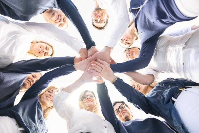 Ein Team steht im Kreis und legt Hand auf Hand