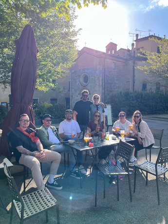 Das Team von Alpenblickdrei genießt gemeinsam einen sonnigen Tag bei einem Drink im Freien, mit einer historischen Gebäudefassade im Hintergrund.