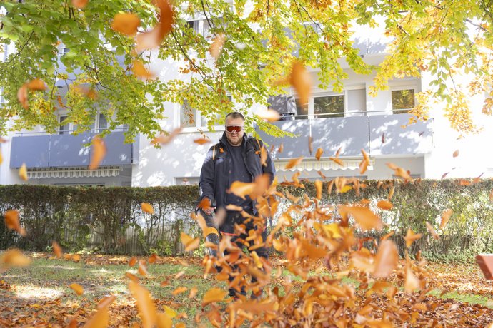 Zwei Personen sitzen auf einer Parkbank unter herbstlich gefärbten Bäumen.