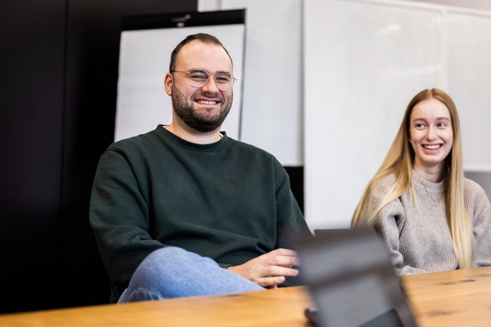 Zweierteam im Austausch Zwei Personen der Alpenblickdrei Werbeagentur sitzen nebeneinander und unterhalten sich freundlich.