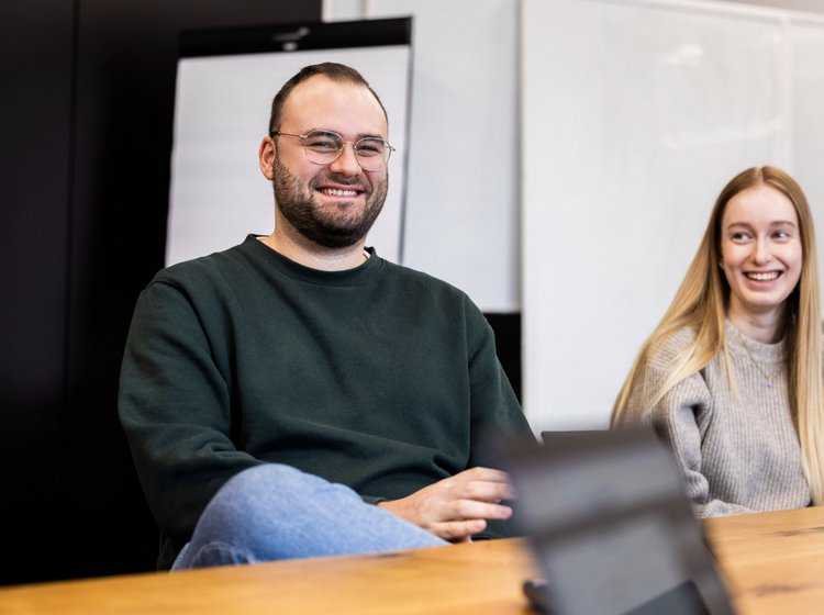 Zwei Personen der Alpenblickdrei Werbeagentur sitzen nebeneinander und unterhalten sich freundlich.