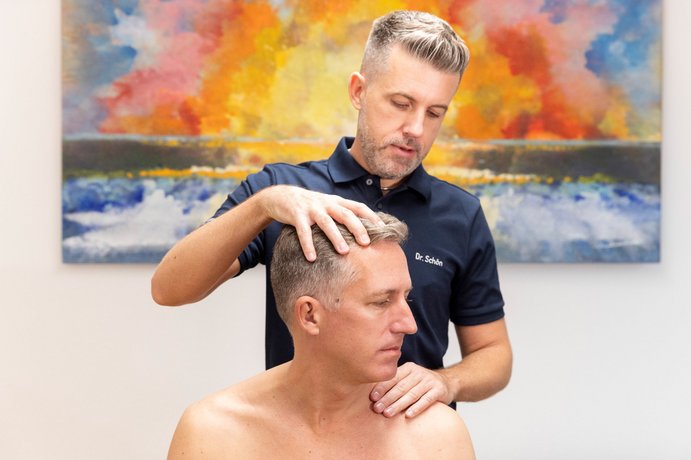 Dr. Schön untersucht einen Mann an der Halswirbelsäule