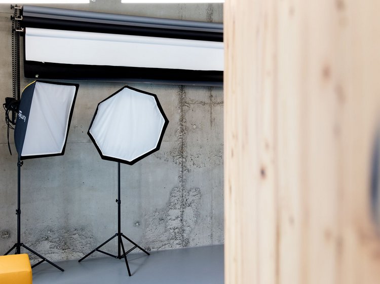 Zwei Studioleuchten mit Softboxen vor einer Betonwand und Fotohintergrundrolle, rechts im Anschnitt eine Holzsäule.