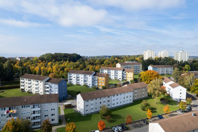 Weitwinkelaufnahme moderner Wohngebäude mit grünen Freiflächen und Parkmöglichkeiten.