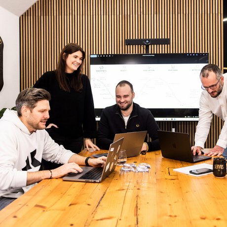 Strategierunde im Konferenzraum Fünf Teammitglieder der Alpenblickdrei Werbeagentur bei einer Besprechung am großen Holztisch.