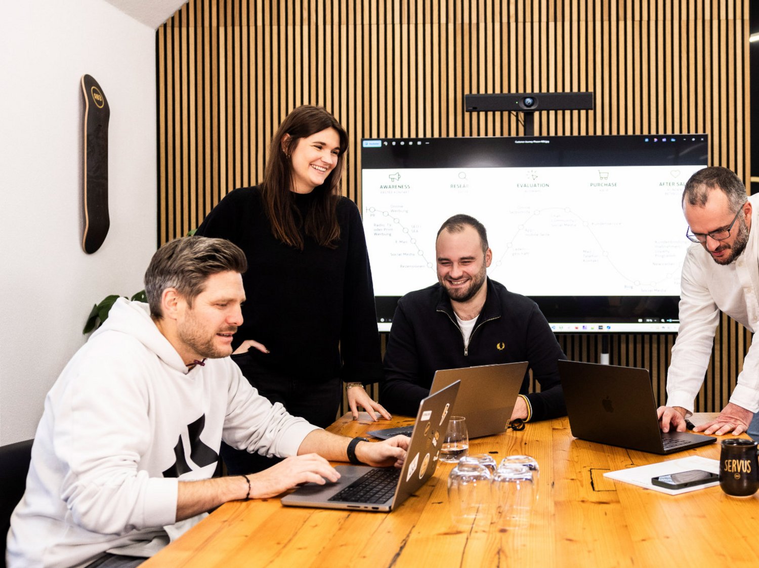 Sechs Teammitglieder der Alpenblickdrei Werbeagentur bei einer Besprechung am großen Holztisch.