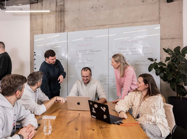 Eine Gruppe von sechs Personen diskutiert an einer Website und arbeitet gemeinsam an einem Design-Projekt. Im