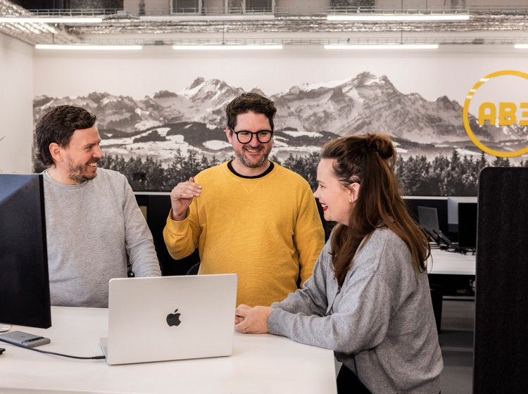 Drei Personen unterhalten sich entspannt in der offenen Küche der Alpenblickdrei Werbeagentur.