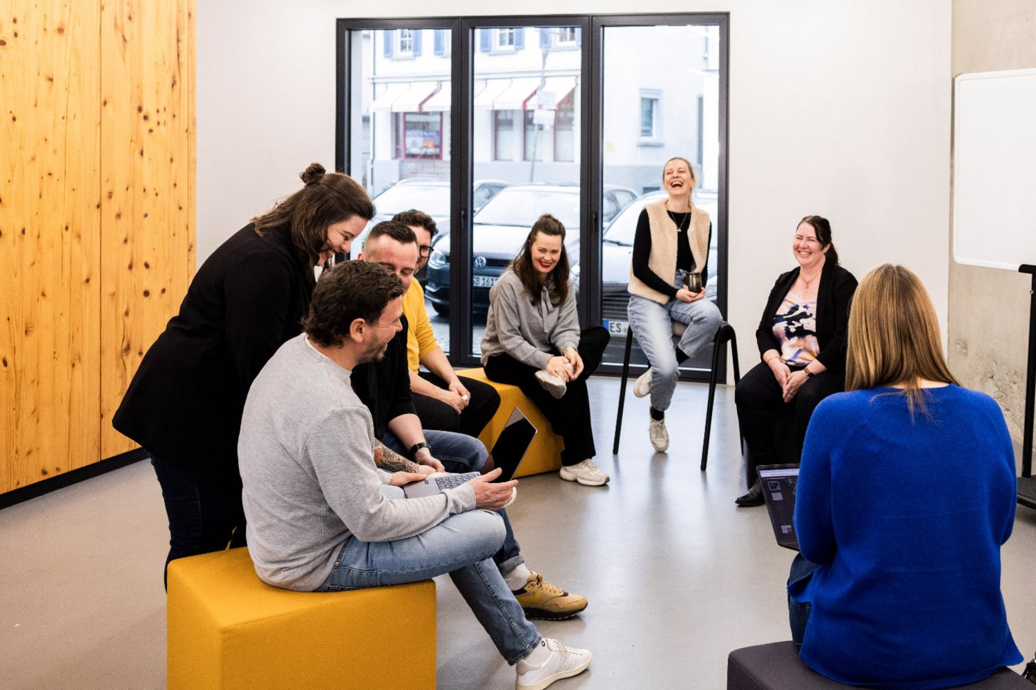 Mehrere Mitarbeitende der Alpenblickdrei Werbeagentur in lockerer Runde mit Sofas und Sesseln im offenen Büro.