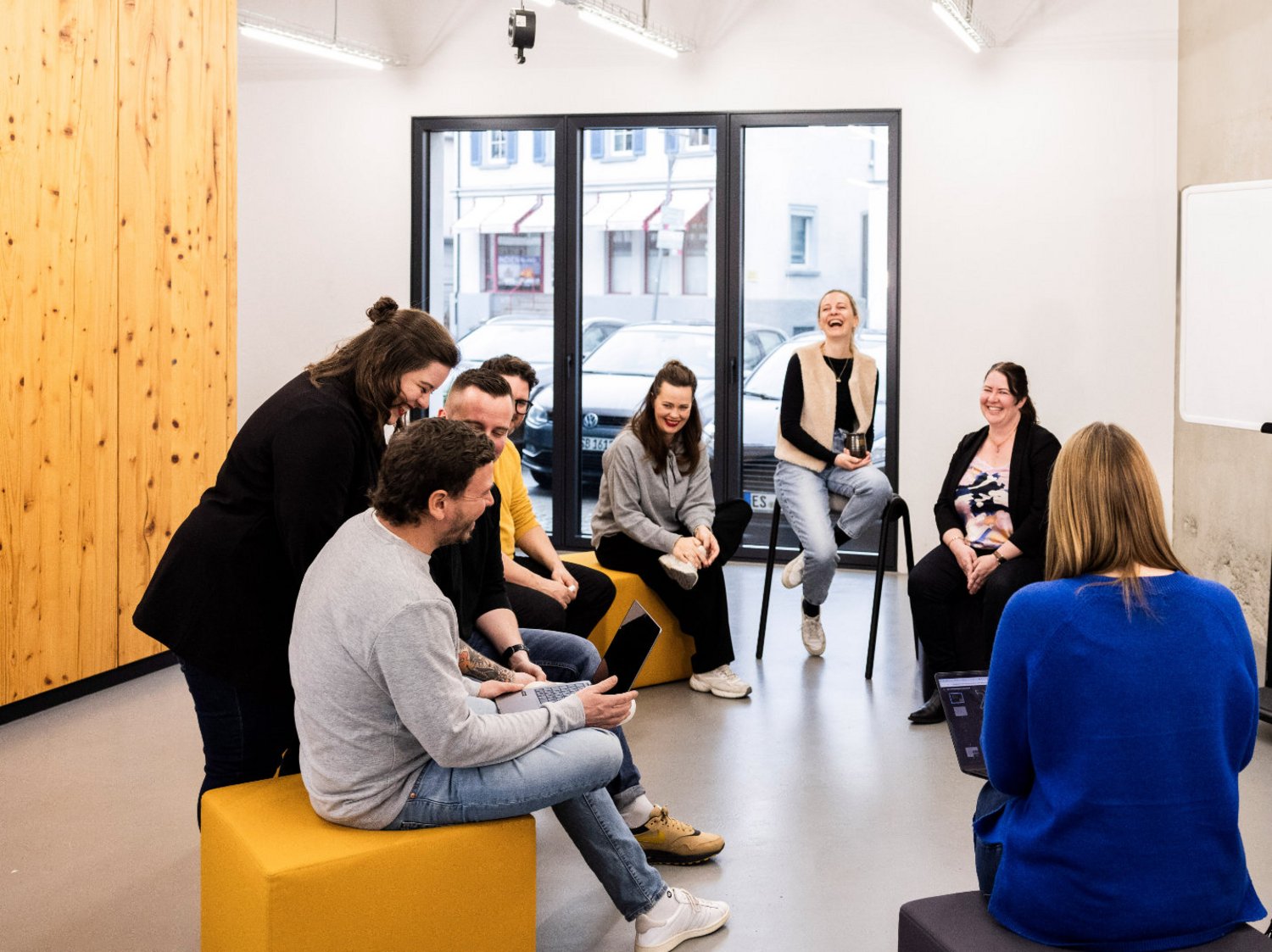 Mehrere Mitarbeitende der Alpenblickdrei Werbeagentur in lockerer Runde mit Sofas und Sesseln im offenen Büro.