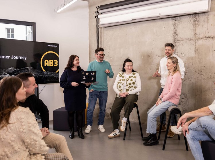 Eine Gruppe von acht Personen bespricht in einem modernen Büro eine Präsentation zum Thema "Customer Journey".