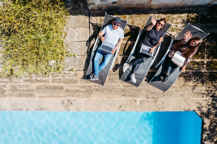 Drei Personen entspannen auf Sonnenliegen neben einem Pool, umgeben von Naturstein und Vegetation, aus der Vogelperspektive aufgenommen.
