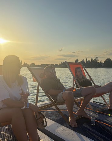 Drei Mitglieder des AB3-Teams entspannen bei Sonnenuntergang in Liegestühlen auf einer schwimmenden Plattform.