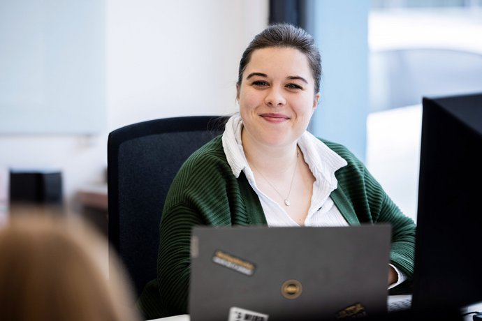 Kollegin im Kundengespräch Mitarbeiterin der Alpenblickdrei Werbeagentur im modernen Büro am Laptop im Austausch mit einer Person.