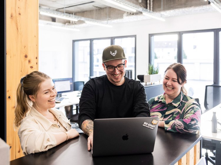 Meeting mit Geschäftsleitung Führungskraft spricht im hellen Besprechungsraum zu mehreren Teammitgliedern der Alpenblickdrei Werbeagentur.