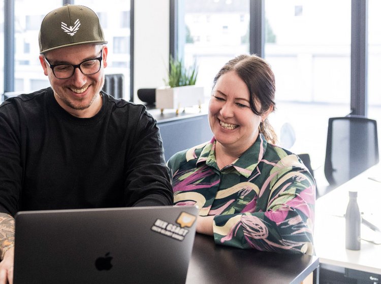 Führungskraft spricht im hellen Besprechungsraum zu mehreren Teammitgliedern der Alpenblickdrei Werbeagentur.