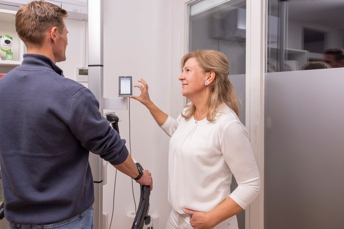 Doreen Alfeld stellt an einem Wandgerät Einstellungen ein, während ein Mann hr zuschaut.
