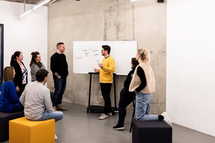 Teammitglied der Alpenblickdrei Werbeagentur schreibt Notizen an ein Whiteboard während eines Workshops.