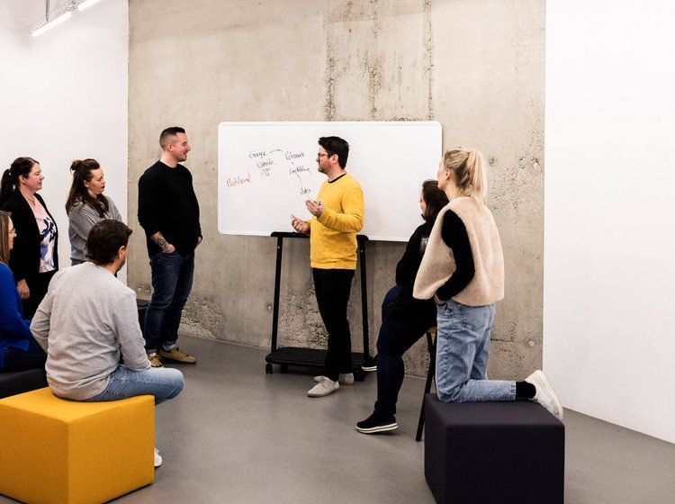 Teammitglied der Alpenblickdrei Werbeagentur schreibt Notizen an ein Whiteboard während eines Workshops.