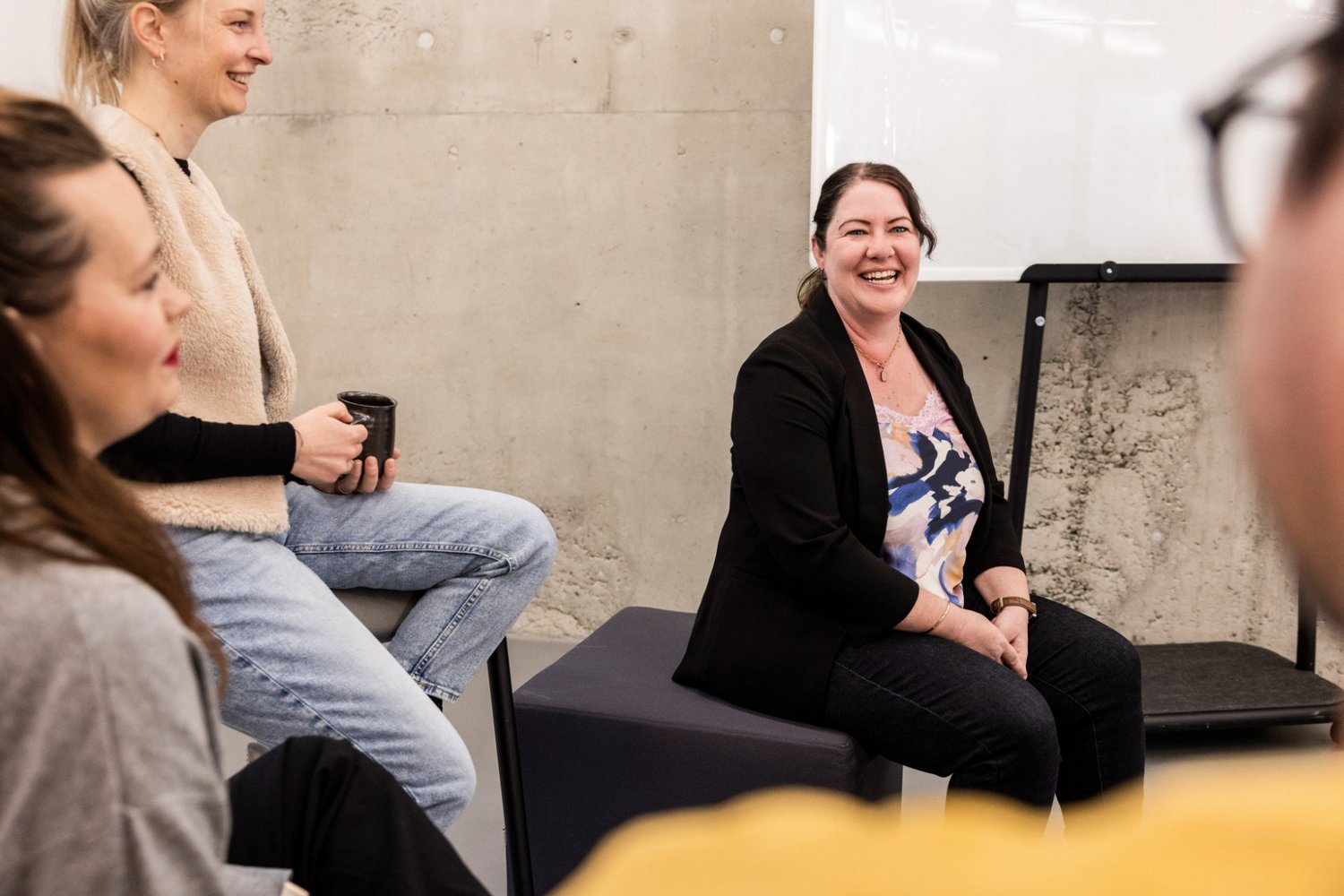 Teammitglied erklärt etwas gegenüber sitzenden Kolleg:innen bei einer lockeren Besprechung im Büro.