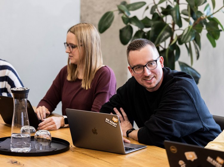 Teamwork am Tisch Drei Mitarbeitende der Alpenblickdrei Werbeagentur lachen gemeinsam bei einer Besprechung.